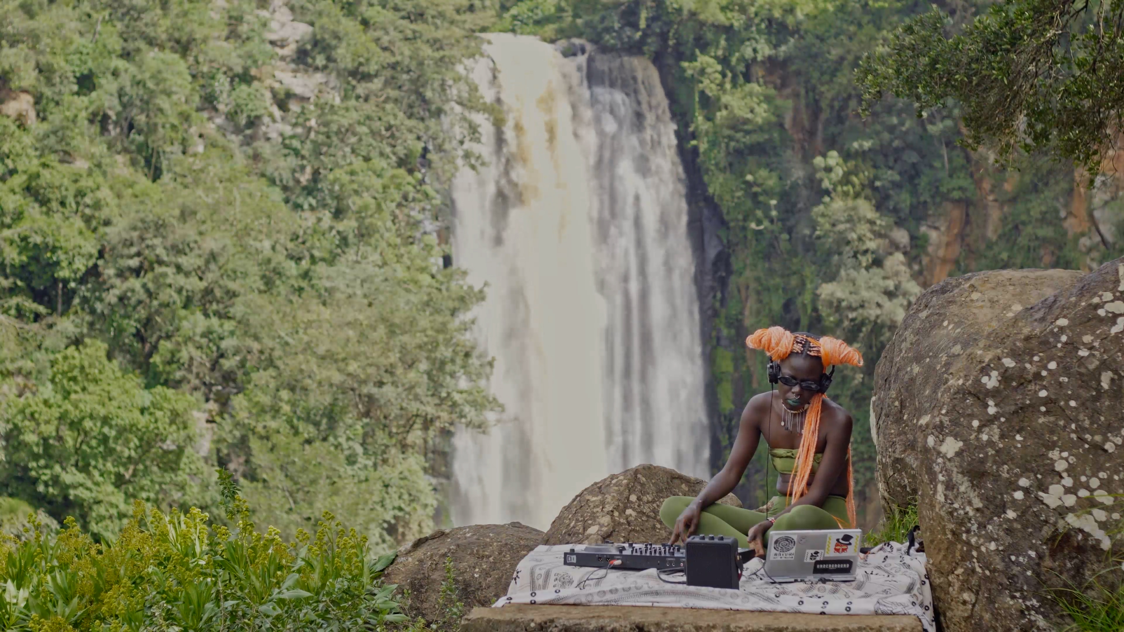 For the artwork “Warm Fronts” by Kent Chan, Makossiri performs near a tropical waterfall. Makossiri is a musician and a DJ.