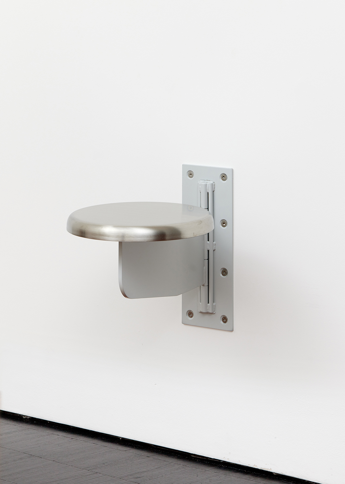A metal stool fixed to the wall. The work is by artist Sung Tieu.